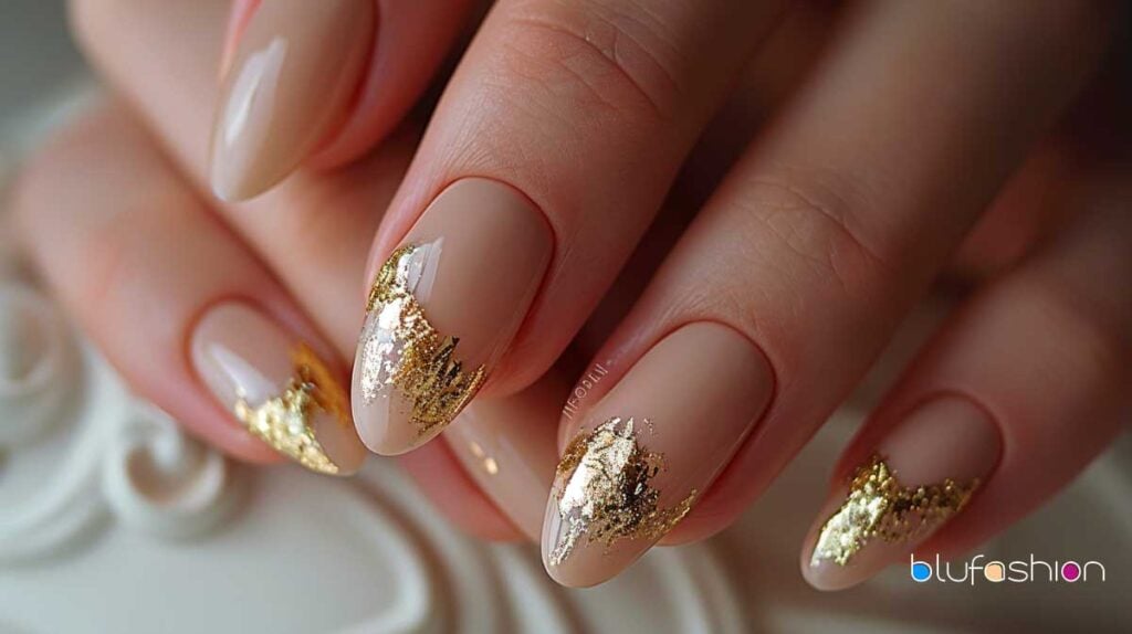 Uñas ovaladas naturales con un elegante esmalte beige y elegantes detalles en pan de oro.