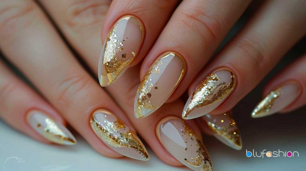Uñas estilo stiletto elegantes con una base beige y detalles en brillo dorado para una apariencia sofisticada.
