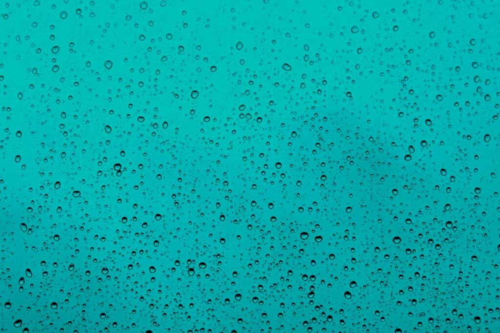 Gotas de lluvia sobre una superficie turquesa creando un patrón texturizado refrescante.