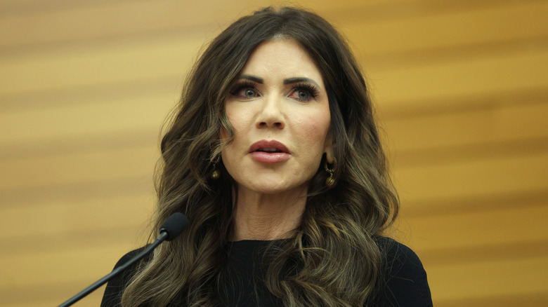 Kristi Noem luciendo un traje negro y joyas de lujo pronuncia un discurso en la Ceremonia de Asunción del Mando