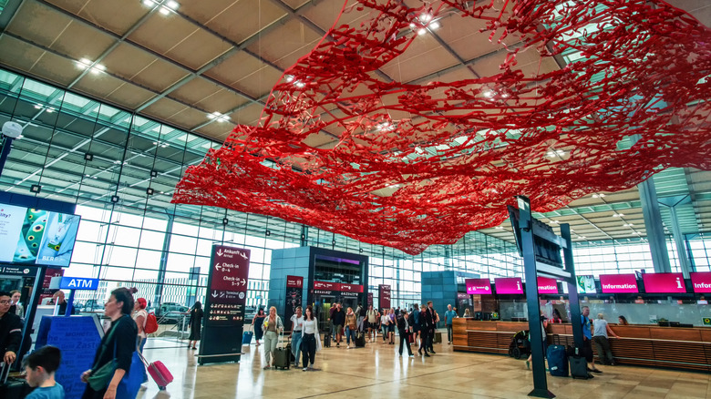 Interior del aeropuerto de Berlín Brandenburgo con viajeros caminando y obras de arte rojas en el techo