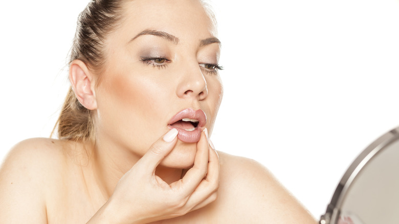 Una mujer inspeccionando sus labios en el espejo.