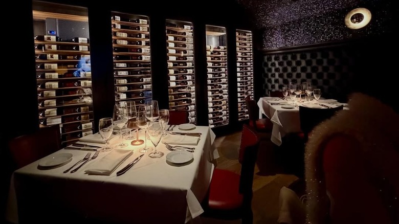 Un comedor con poca luz, botellas de vino y mesas puestas en Durant's Steakhouse