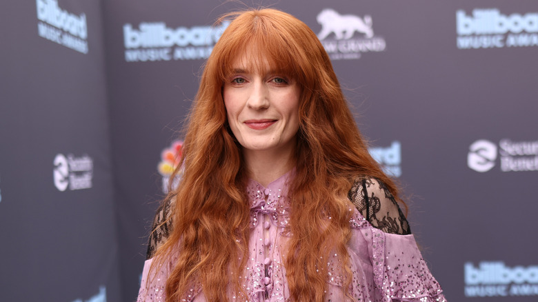 Florence Welch sonríe en un evento de alfombra roja mientras luce un vestido rosa claro con mangas de encaje