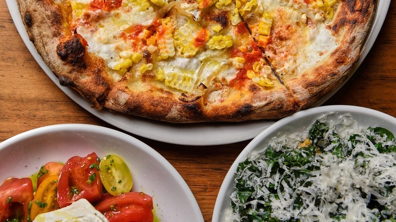 Comida típica italiana: pizza artesanal cubierta con salsa de tomate, mozzarella y maíz, tomates cherry y mozzarella y pimientos verdes asados ​​cubiertos con queso rallado.