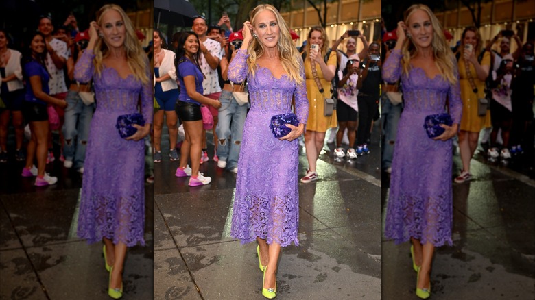 Sarah Jessica Parker posando en un evento en 2023 con la mano en la cabeza y luciendo un vestido de encaje morado.