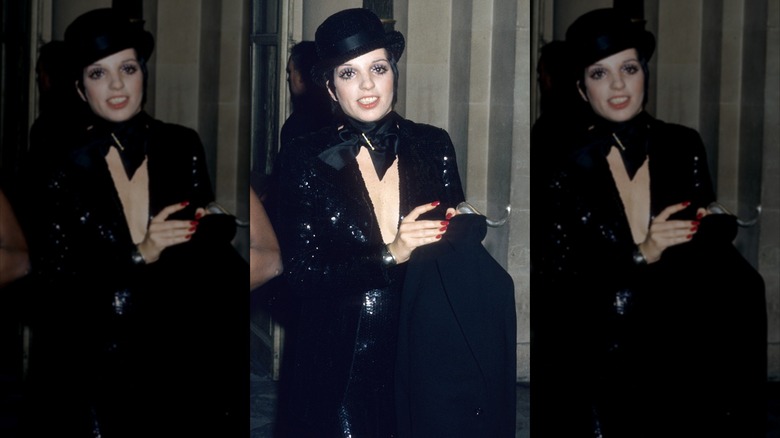 Liza Minnelli luce un traje brillante completamente negro con un bombín negro.