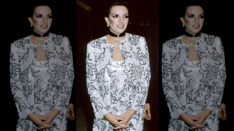 Liza Minnelli posa con las manos entrelazadas luciendo un conjunto blanco y negro y una gargantilla negra.