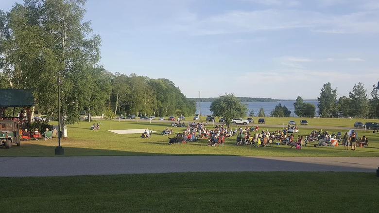 Una multitud reunida en el césped del Centro Erickson para las Artes en Curtis, Michigan, con un lago al fondo