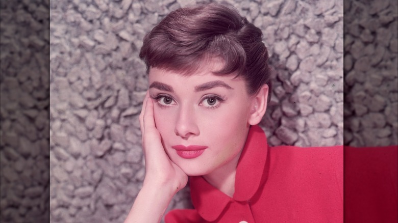 Audrey Hepburn posando con la cabeza entre las manos y luciendo un top rojo