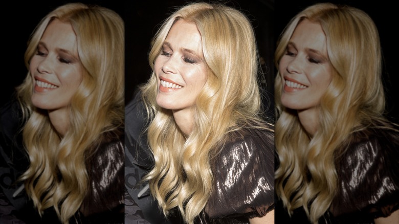 Claudia Schiffer sonriendo con los ojos cerrados con un top metálico brillante y el pelo rizado suelto.