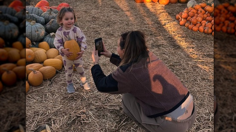 Kaley Cuoco se agacha para tomar una foto de su hija Matilda en un huerto de calabazas.