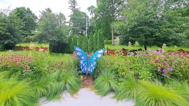 Un jardín dentro de Matter Park en Indiana, con flores coloridas y una gran instalación artística de mariposas azules, rodeado de exuberante vegetación.