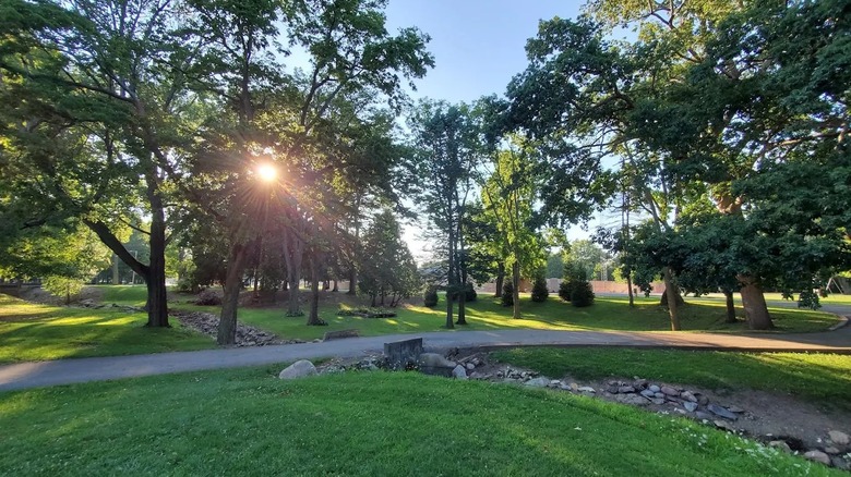 Matter Park en Indiana, con césped exuberante con senderos pavimentados, elementos de piedra y el sol brillando entre los árboles.