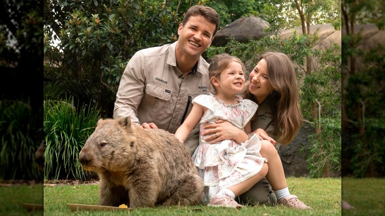 Bindi Irwin sosteniendo a su hija posando junto a su marido y un wombat.