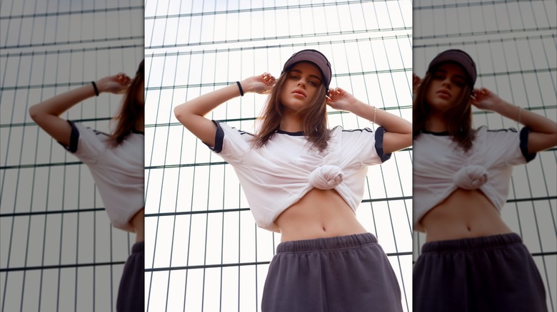 Una mujer posando con un top corto anudado blanco y azul marino y pantalones deportivos.