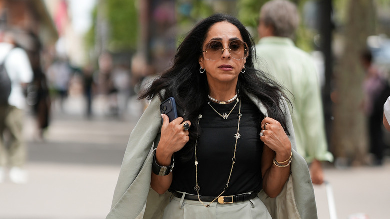 Una mujer viste una chaqueta, una camiseta negra y un collar llamativo.
