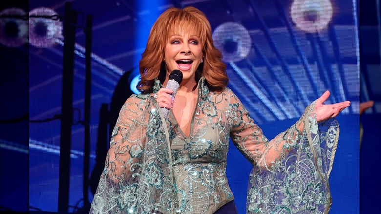 Reba McEntire usa un top turquesa detallado mientras canta frente a un micrófono deslumbrante en el escenario.