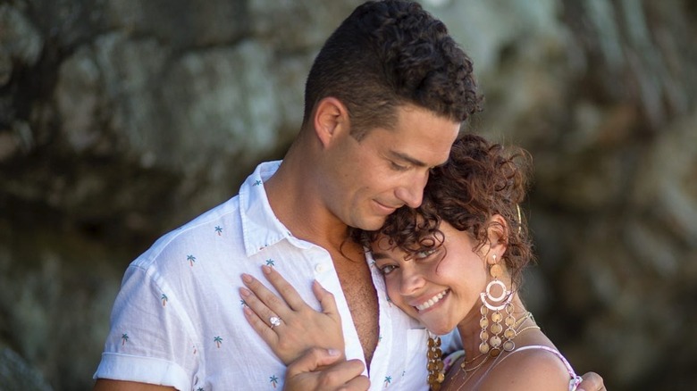 Wells Adams con una camisa blanca con botones mirando a Sarah Hyland mientras se abrazan.