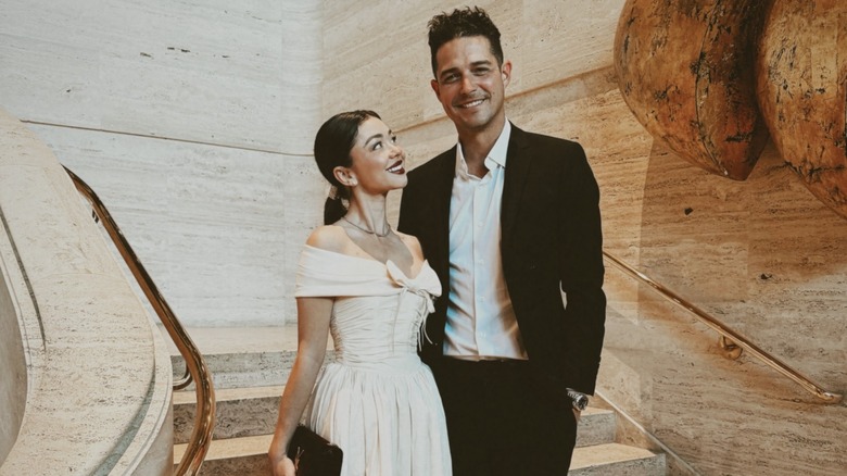 Sarah Hyland con un vestido color crema y una cola de caballo peinada hacia atrás junto a Wells Adams con un traje negro.
