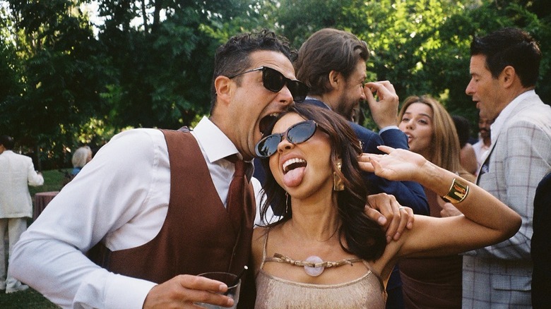 Wells Adams con chaleco marrón y corbata con botones blancos mordiendo la cabeza de Sarah Hyland