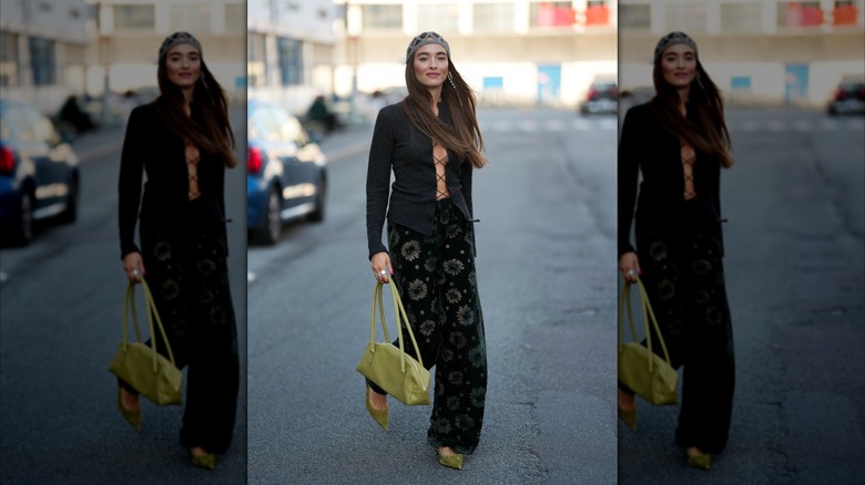 Una mujer vestida con pantalones de terciopelo de flores, tacones de terciopelo verde y una blusa negra con cordones.