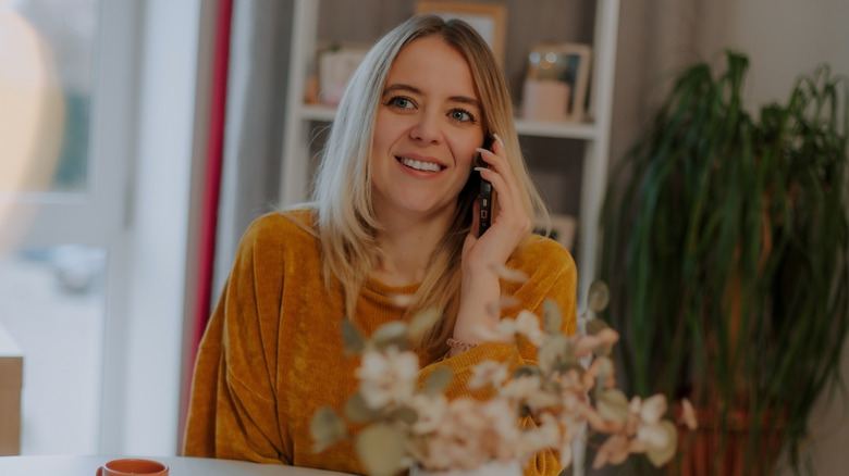 Una mujer vistiendo un suéter amarillo mostaza mientras habla por teléfono