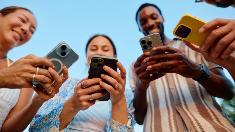 Cuatro adultos jóvenes que operan teléfonos inteligentes