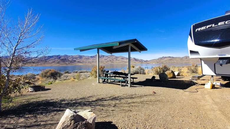 Vista parcial de una casa rodante en un campamento frente al mar en el Área Recreativa Estatal Wild Horse en Nevada, que cuenta con un área de picnic con sombra y una fogata.
