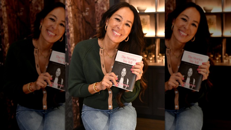 Joanna Gaines posando con su libro vestida con jeans y un suéter verde oscuro.