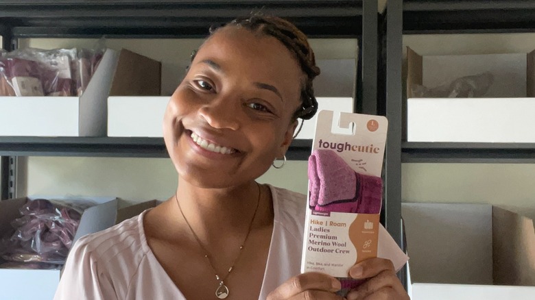 La fundadora de ToughCutie, Brittany Coleman, lleva el pelo recogido junto con una camiseta rosa claro y pequeños aros mientras muestra un nuevo color de calcetines en julio de 2025.