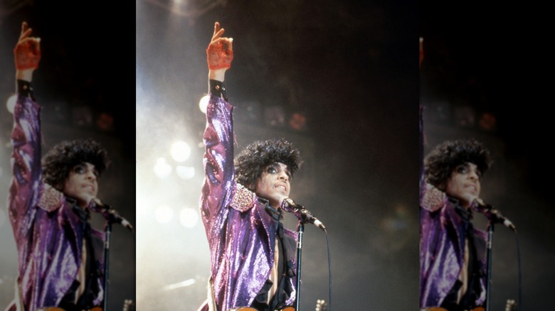 Prince actuando durante la gira Purple Rain con una chaqueta morada brillante y la mano en el aire.
