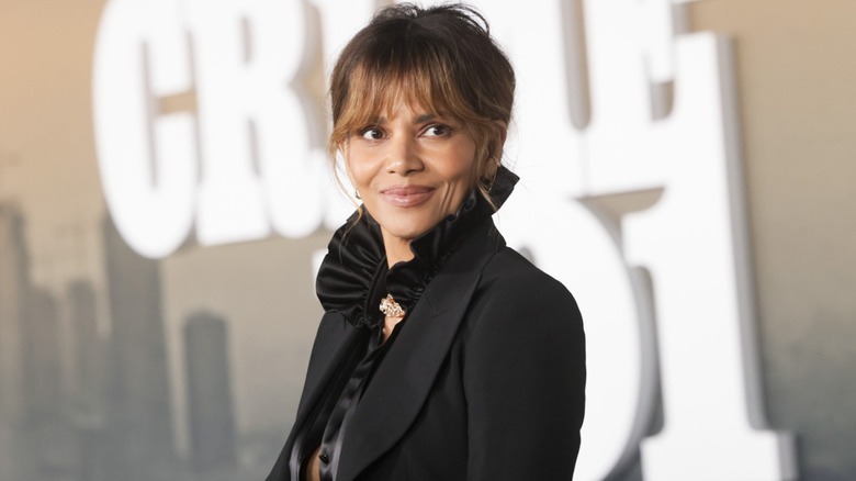Halle Berry en un evento con el pelo recogido luciendo una chaqueta negra y una blusa negra con escote de volantes.