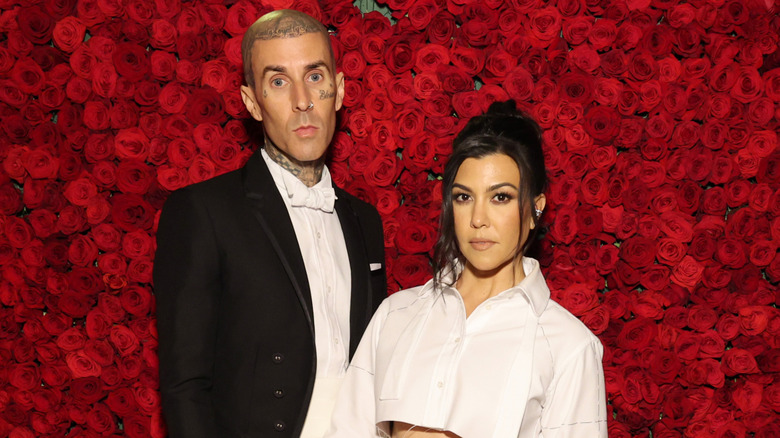 Travis Barker y Kourtney Kardashian posan frente a una pared de rosas rojas