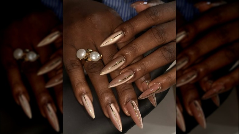 Manicura de punta larga con esmalte de uñas de ojo de gato dorado y diseños de rayas doradas.