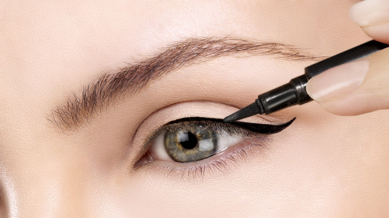 Primer plano de una persona que se aplica un delineador de ojos negro con el ojo abierto
