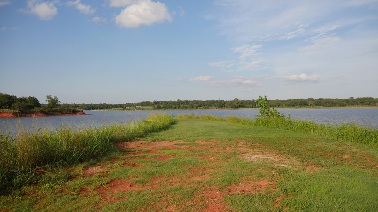 Suelo rojo cubierto de hierba frente a las aguas azules del lago Stanley Draper en Oklahoma City, Oklahoma