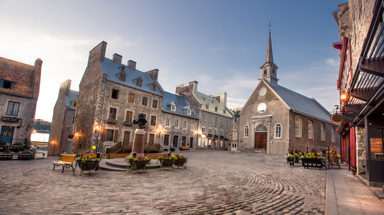 Una vista de una calle histórica del Viejo Quebec con el campanario de una iglesia que se eleva sobre una plaza empedrada.