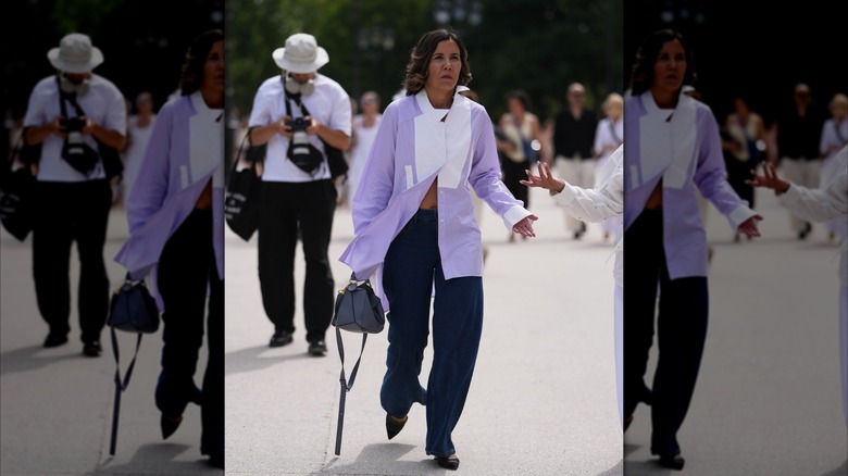 Una mujer viste jeans oscuros y una camisa con botones de color morado claro y blanco.