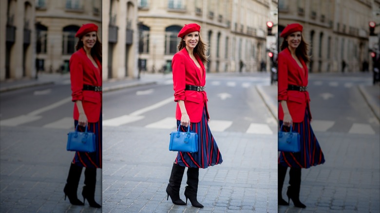 Una mujer vestida con una chaqueta roja, cinturón negro y una falda de rayas azules y rojas.