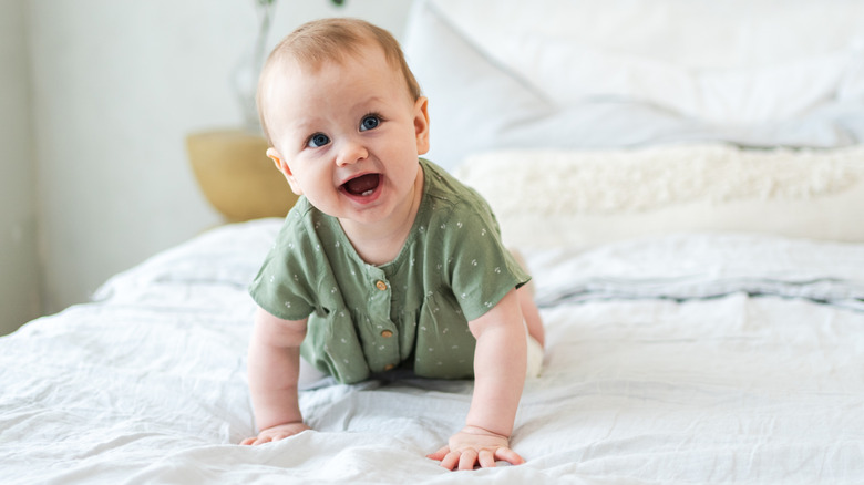 Bebé riendo gateando sobre una cama