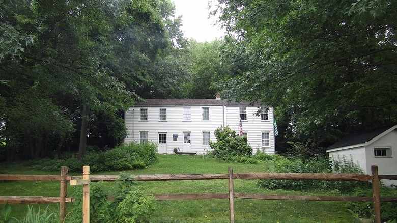 Rachel Carson Homestead, una casa de dos pisos con revestimiento blanco rodeada de césped y árboles, detrás de una valla de madera.