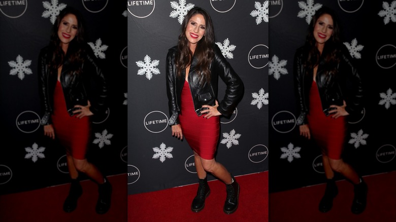 Soleil Moon Frye posando en un evento de alfombra roja con un vestido rojo ajustado con una chaqueta de cuero negra y botas negras.