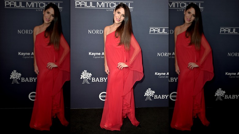 Soleil Moon Frye posando en un evento de alfombra roja con un vestido rojo de un solo hombro y una manga transparente y fluida.