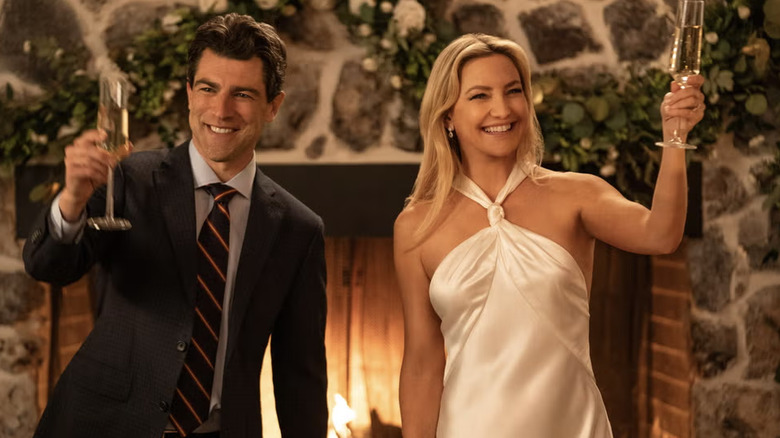 Kate Hudson con un vestido marfil con cuello halter Galvan de pie junto a Max Greenfield sosteniendo copas de champán.