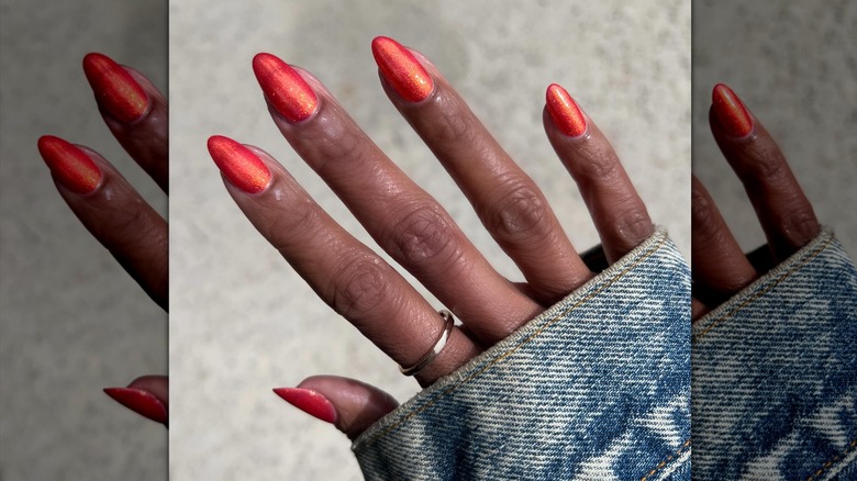 Una mano con esmalte de uñas brillante de color naranja quemado.