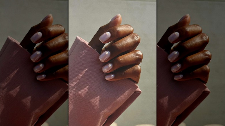 Una mano con esmalte de uñas rosa nude con detalles en perlas.