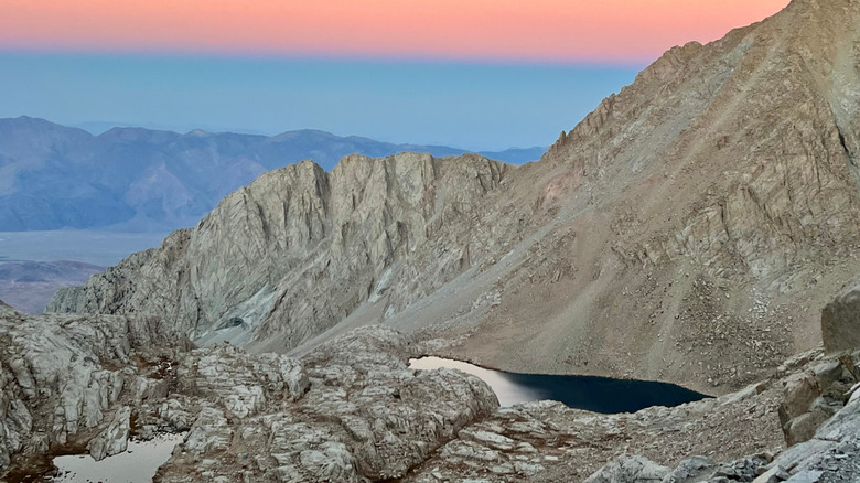Montañas de granito grisáceo que rodean el lago Consultation con un cielo rosa y azul arriba y montañas al fondo