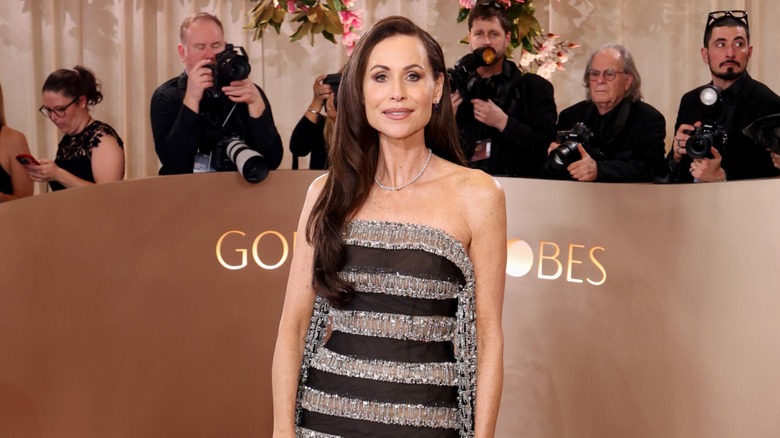 Minnie Driver posando en la alfombra roja con un vestido de rayas negras y plateadas.