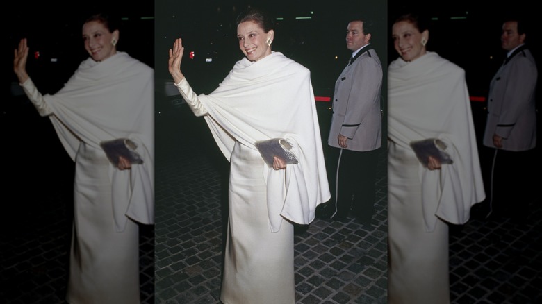 Audrey Hepburn en los Globos de Oro luciendo un vestido blanco con un chal blanco, saludando a las cámaras.